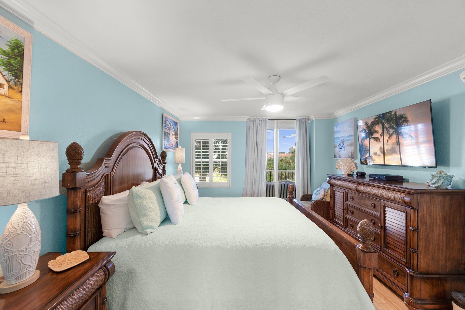 A bedroom with a large bed, a wooden dresser, a television, and a window with curtains.