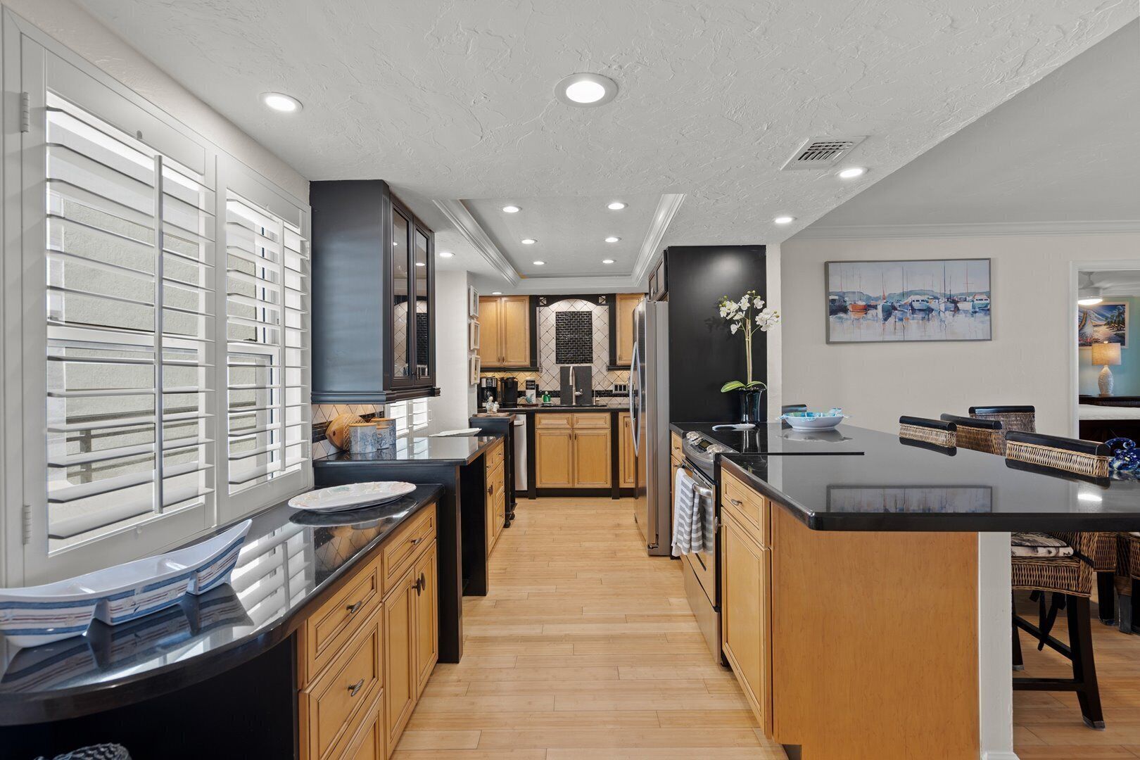 A modern kitchen with a central island, wooden cabinets, and a large window with blinds.