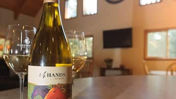 A bottle of wine on a table with glasses around it, in a room with windows and a clock on the wall.