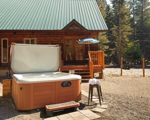 A wooden cabin with a hot tub, a deck, and a covered seating area.