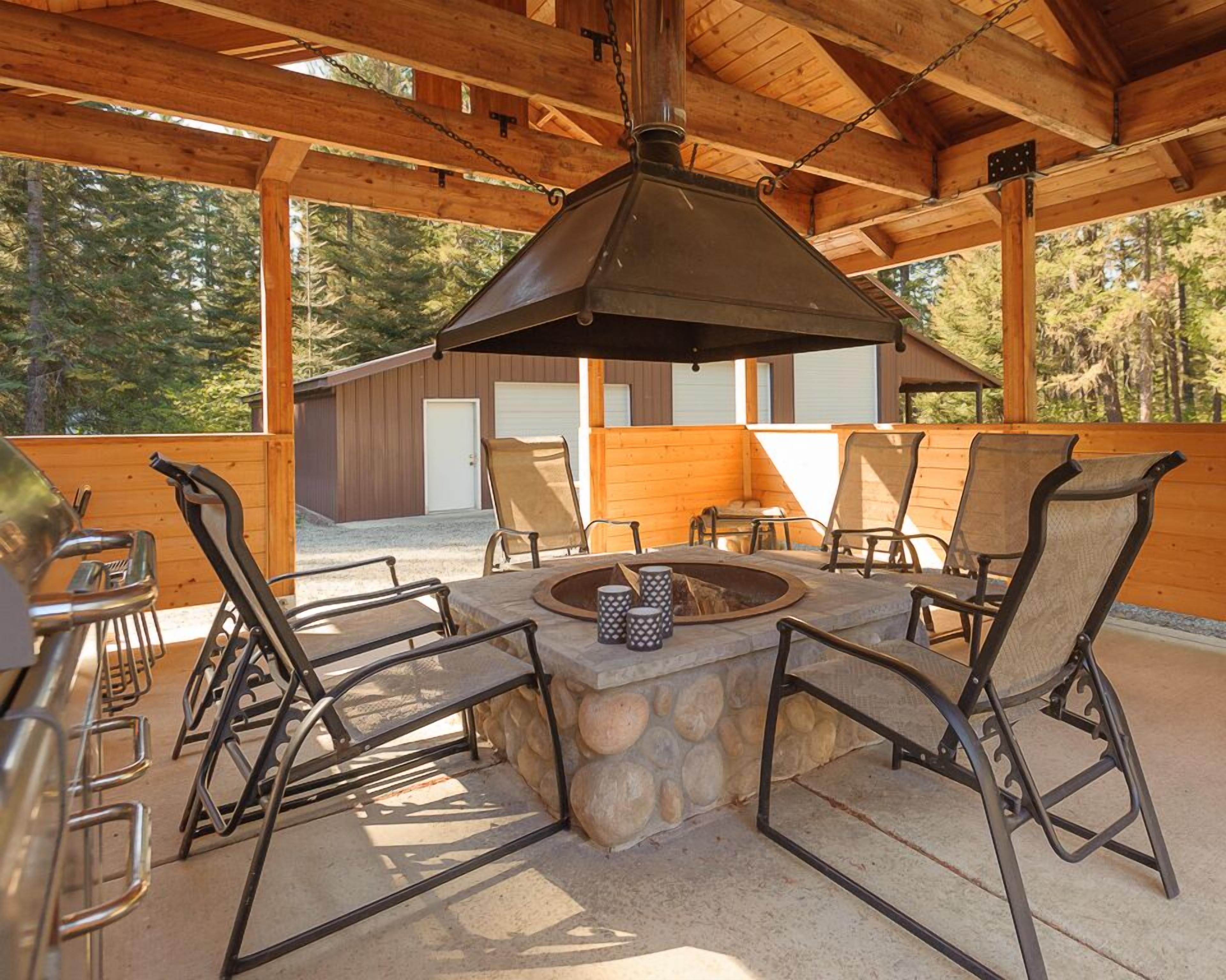 Une terrasse extérieure avec un foyer en pierre, des chaises en métal et un barbecue.
