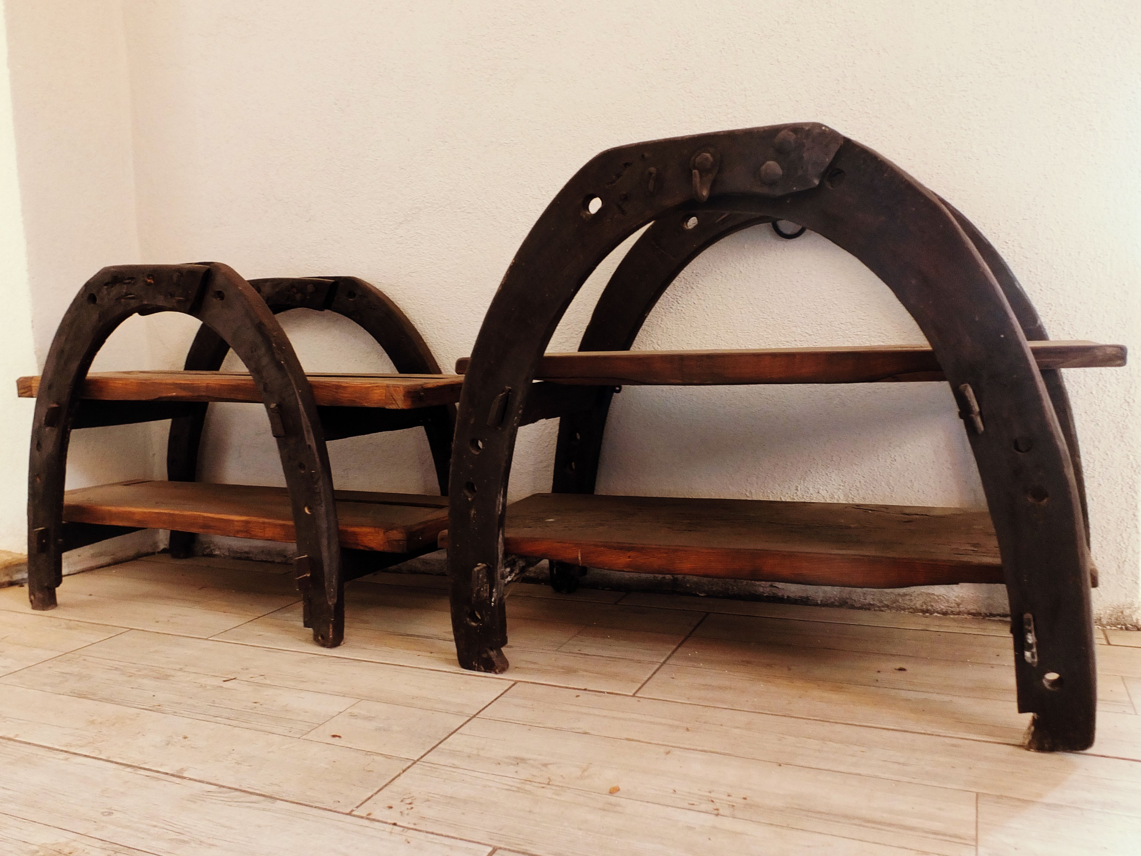 Zwei hölzerne Bänke mit Metallbögen, vor einer schlichten Wand auf Fliesen.