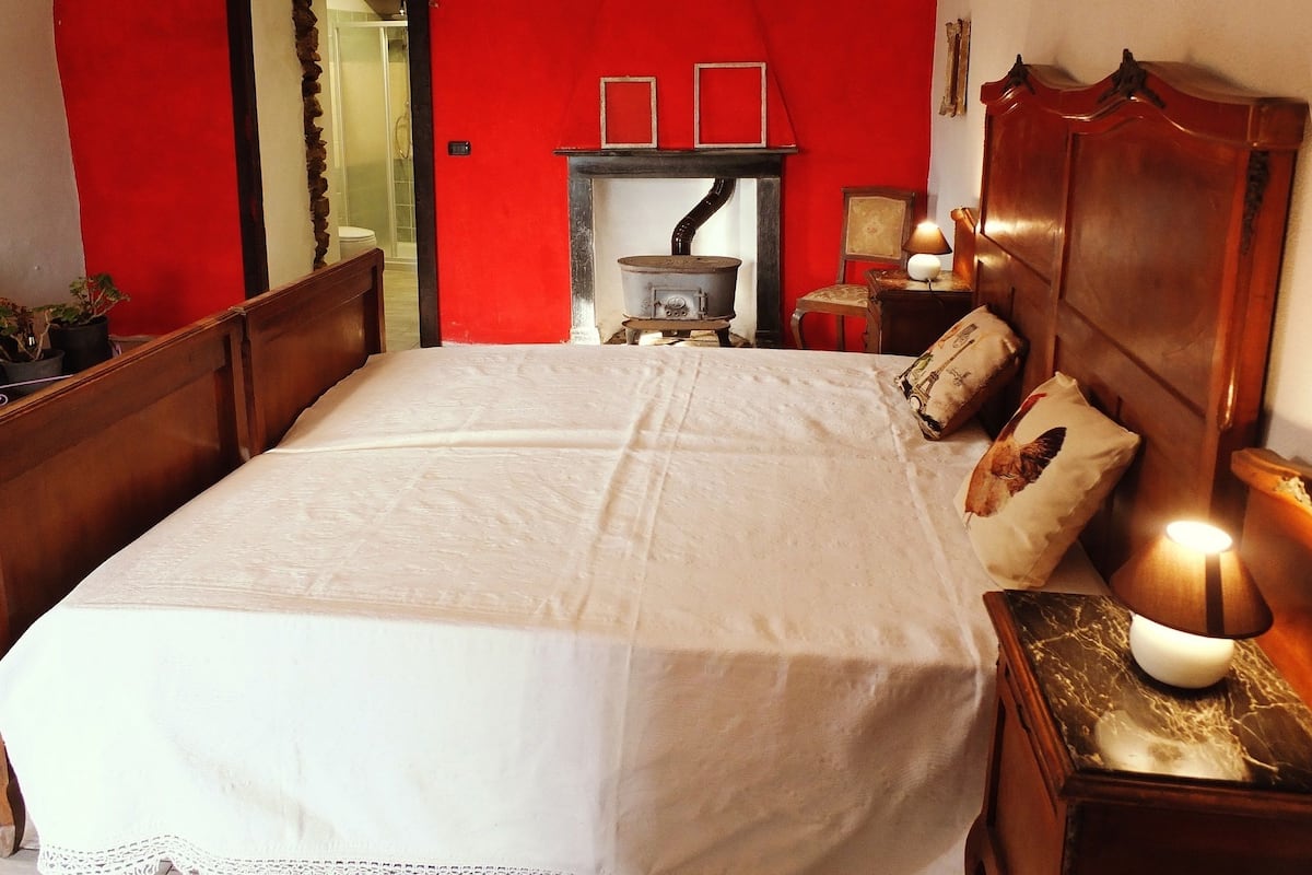 Un dormitorio con una cama grande, un cabecero de madera, una mesita de noche con lámpara, una pequeña mesa con lámpara y una pared roja.