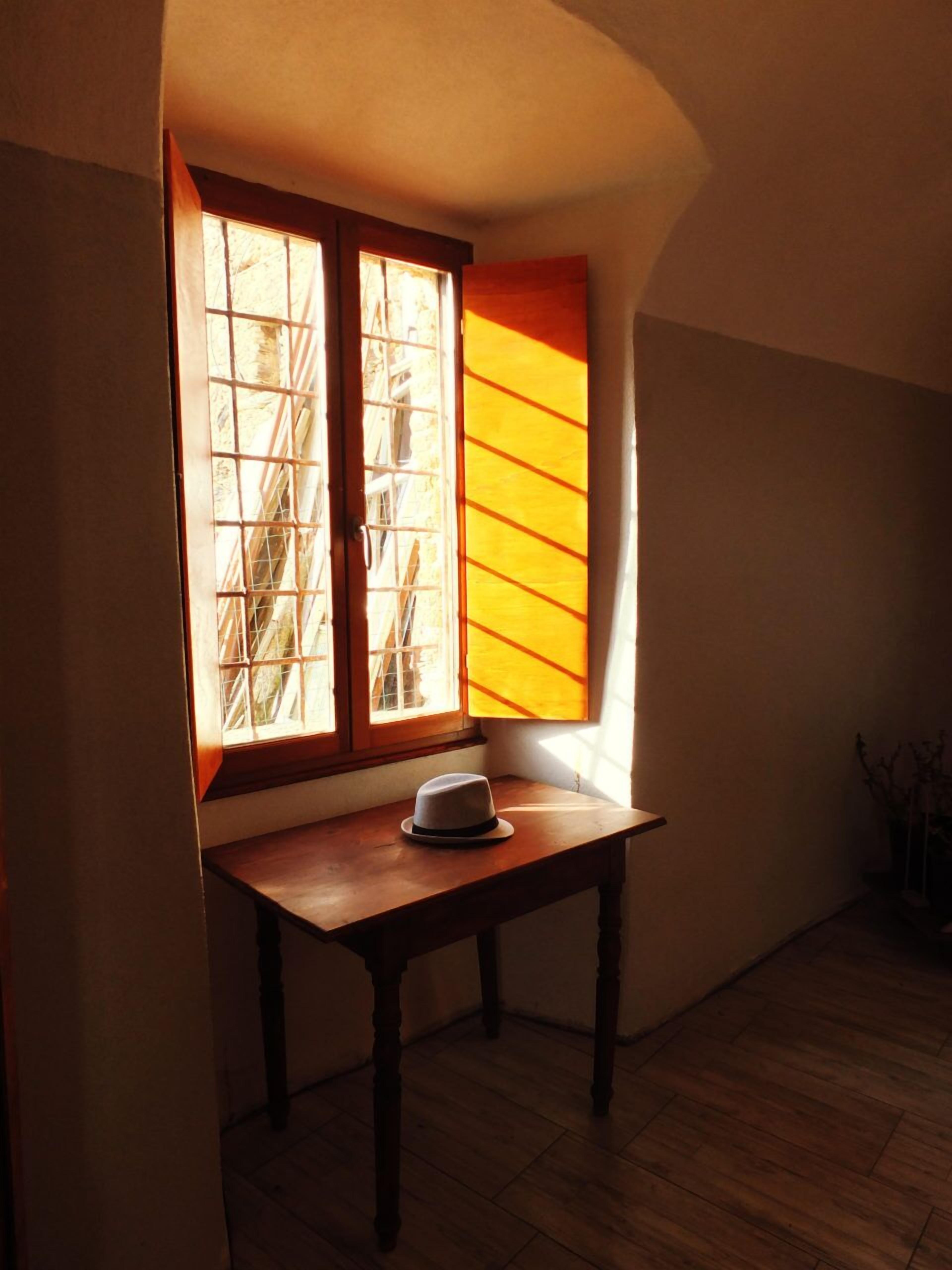 Une pièce avec une table en bois, un chapeau posé sur la table et une fenêtre donnant sur l’extérieur.