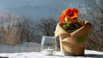 A candle in a glass jar, a bouquet of orange flowers in a burlap sack, and a tablecloth on a wooden table with a mountainous backdrop.