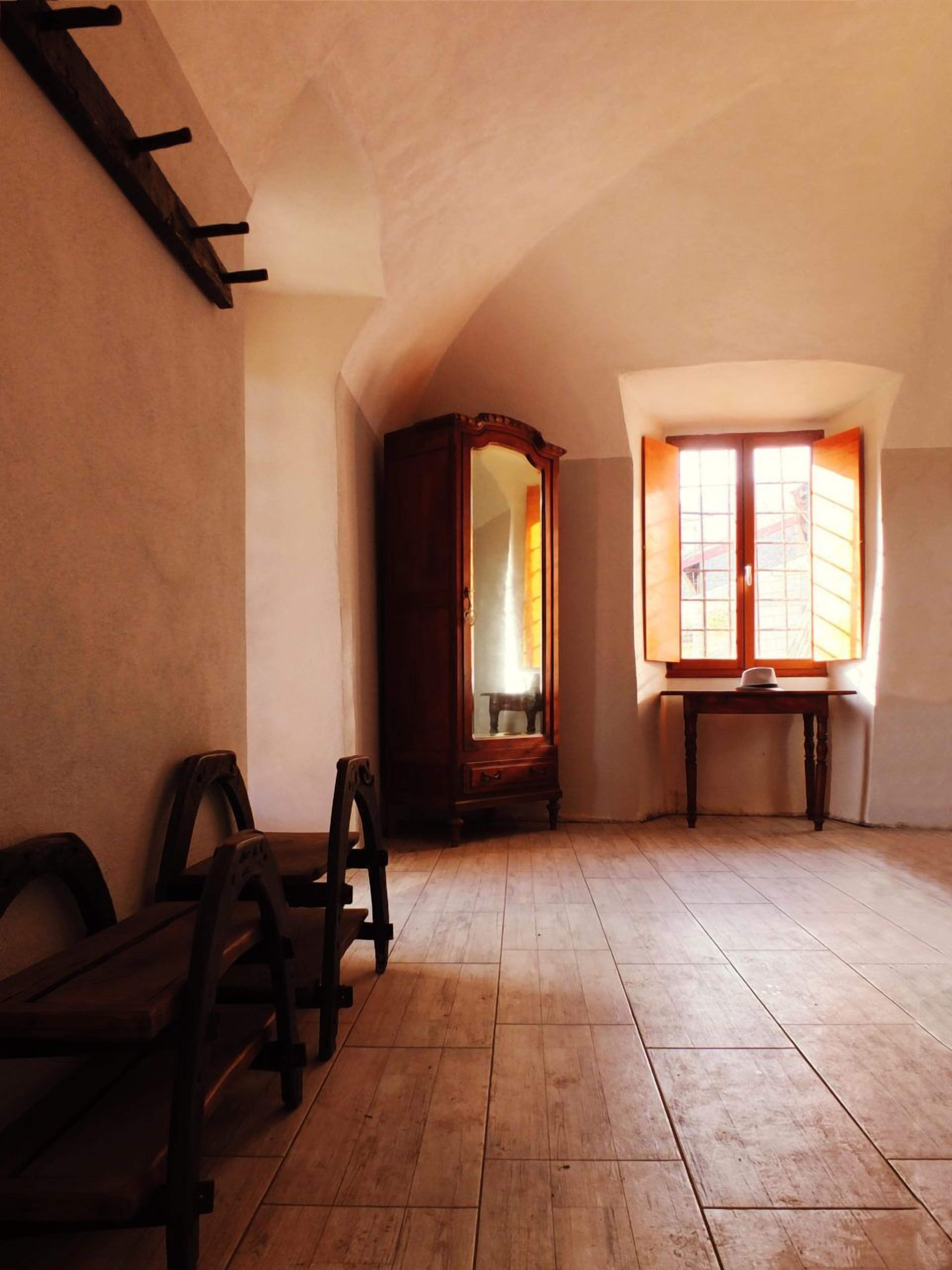 A room with wooden flooring, a large mirror, a wooden wardrobe, and a window with curtains.