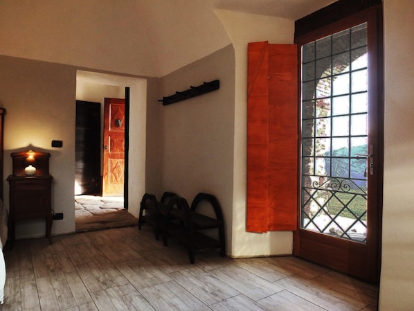 Una habitación con suelo de madera, un banco de madera, una puerta con panel de vidrio y un estante fijado a la pared.