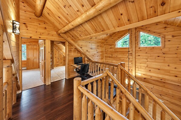 A wooden interior with a staircase, a desk with a computer, and a window.