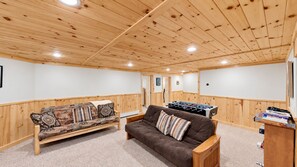 A cozy room with a wooden ceiling, a sofa, a brown couch, and a foosball table.