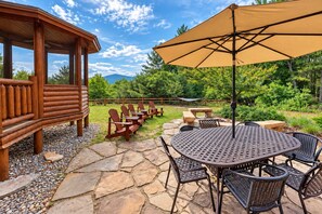A wooden cabin with a patio area featuring a table, chairs, and an umbrella. - Grand Jay Lodge, Ultimate Log Luxury, Stunning Views, Hot Tub & Sauna, EV Charger, 3D Tour (Jay)