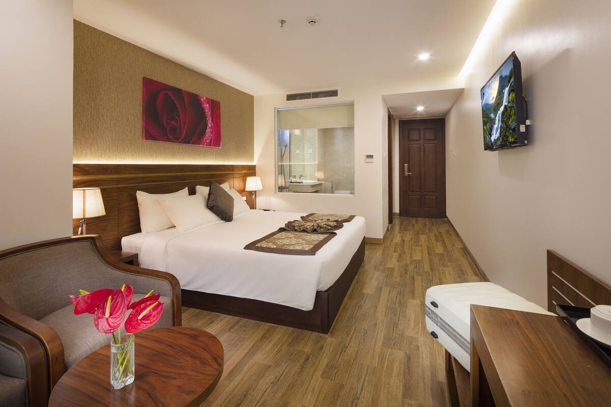 A hotel room with a bed, bedside table, chair, and a TV mounted on the wall.