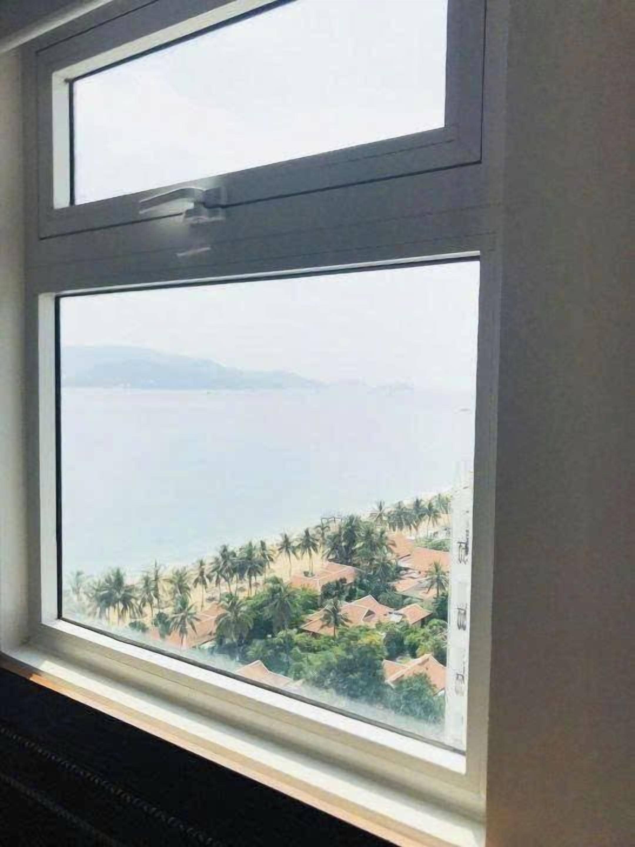 A window with a view of a coastal area, including houses and palm trees.