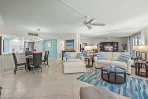 A modern living room with a dining area, a ceiling fan, and a large window. - Crystal Sands Tower Unit 704 - Beachfront (Sarasota)