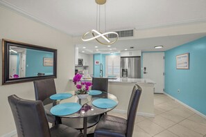 A dining area with a glass table, blue placemats, and purple flowers. - Crystal Sands Tower Unit 704 - Beachfront (Sarasota)