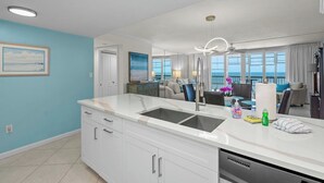 Cozinha moderna com ilha central, área de refeições com vista e sala de estar com varanda.