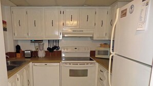 A compact kitchen with white cabinets, a dishwasher, an oven, a microwave, and a refrigerator. - SEASIDE ESCAPE ON ST. AUGUSTINE BEACH - WHERE OLD IS NEW AGAIN!!! (St Augustine Beach)