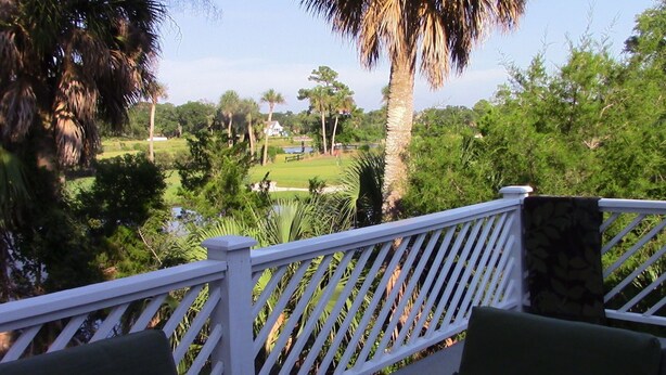 A deck with white railings overlooking a golf course and a pond.