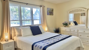Un dormitorio con cama, mesitas de noche, cómoda, espejo y ventana con cortinas.