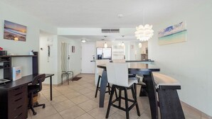 A modern kitchen with a central island, a dining area with chairs, and a workspace with a desk and chair. - Crystal Sands Tower Unit 805 - Beachfront (Sarasota)