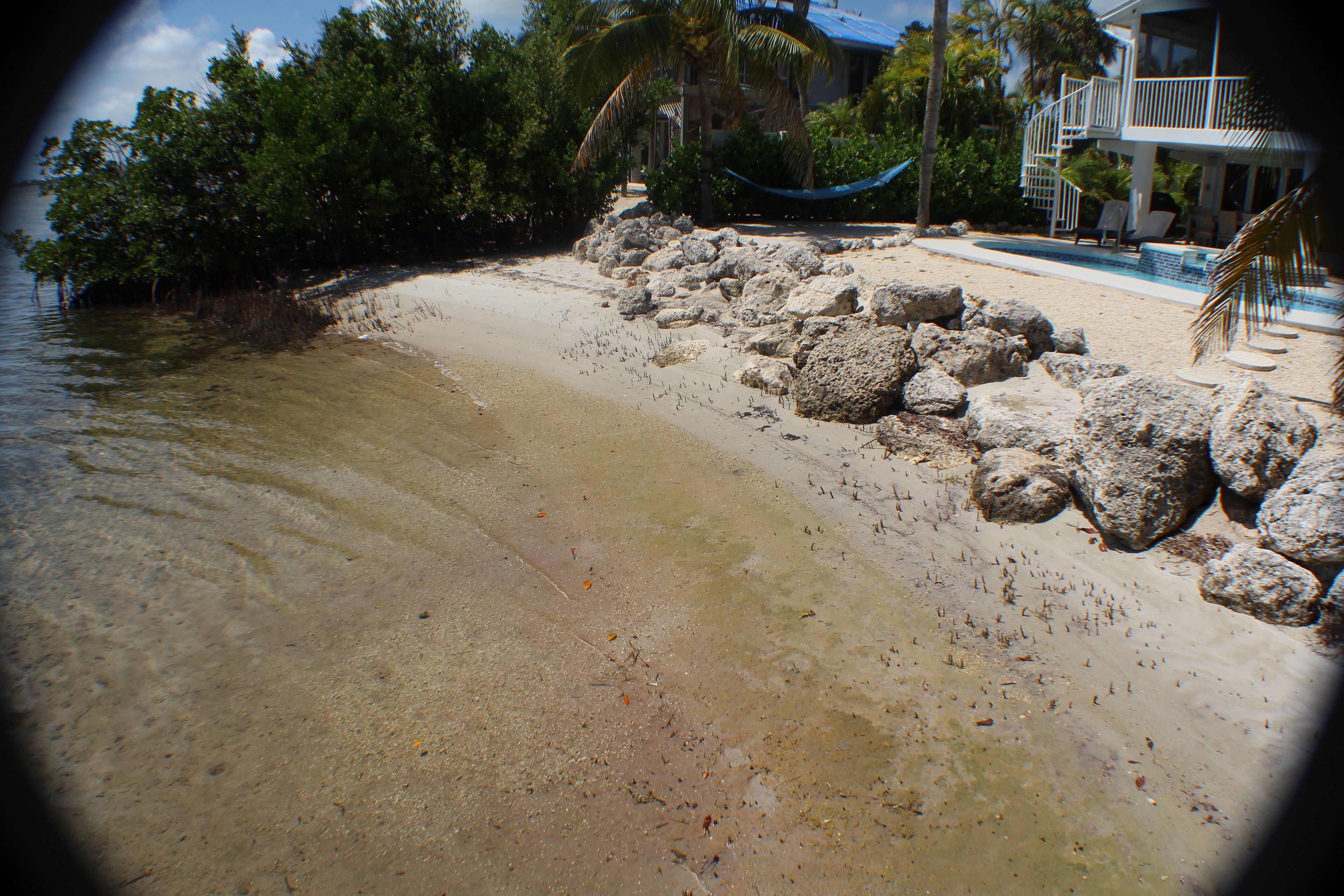 A beach with large rocks, a pool, and a house in the background.