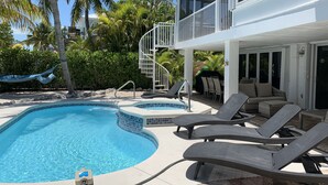 Un espace piscine comprenant des chaises longues, un jacuzzi et un escalier menant à un balcon.