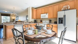 A modern kitchen with wooden cabinets, a central island, and a dining area with chairs and a table set for four. - Vista Cay Resort Townhome near Convention/Universal/SeaWorld/Single Greek Golf (Orlando)