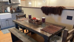 A wooden dining table with benches, a kitchen area with a microwave, and a hanging fur throw. - Romantic Retreat for Two: Make A Montana Memory! (Livingston)