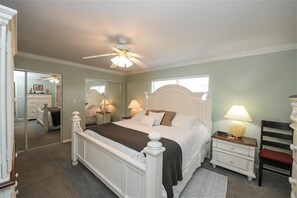 Classic bedroom with a large bed, nightstand, and wooden chair, featuring a spacious bathroom through an open door.