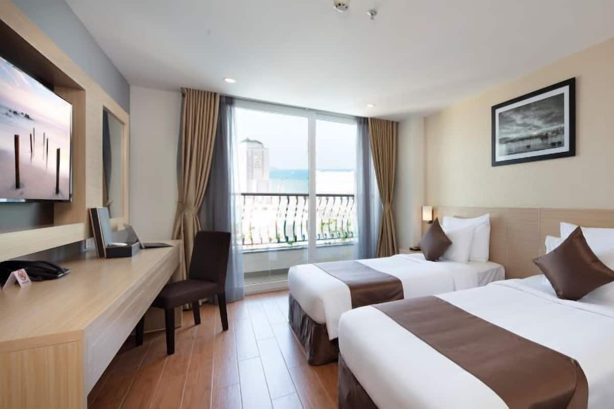 A hotel room with two beds, a desk, a chair, a TV, and a window with curtains.