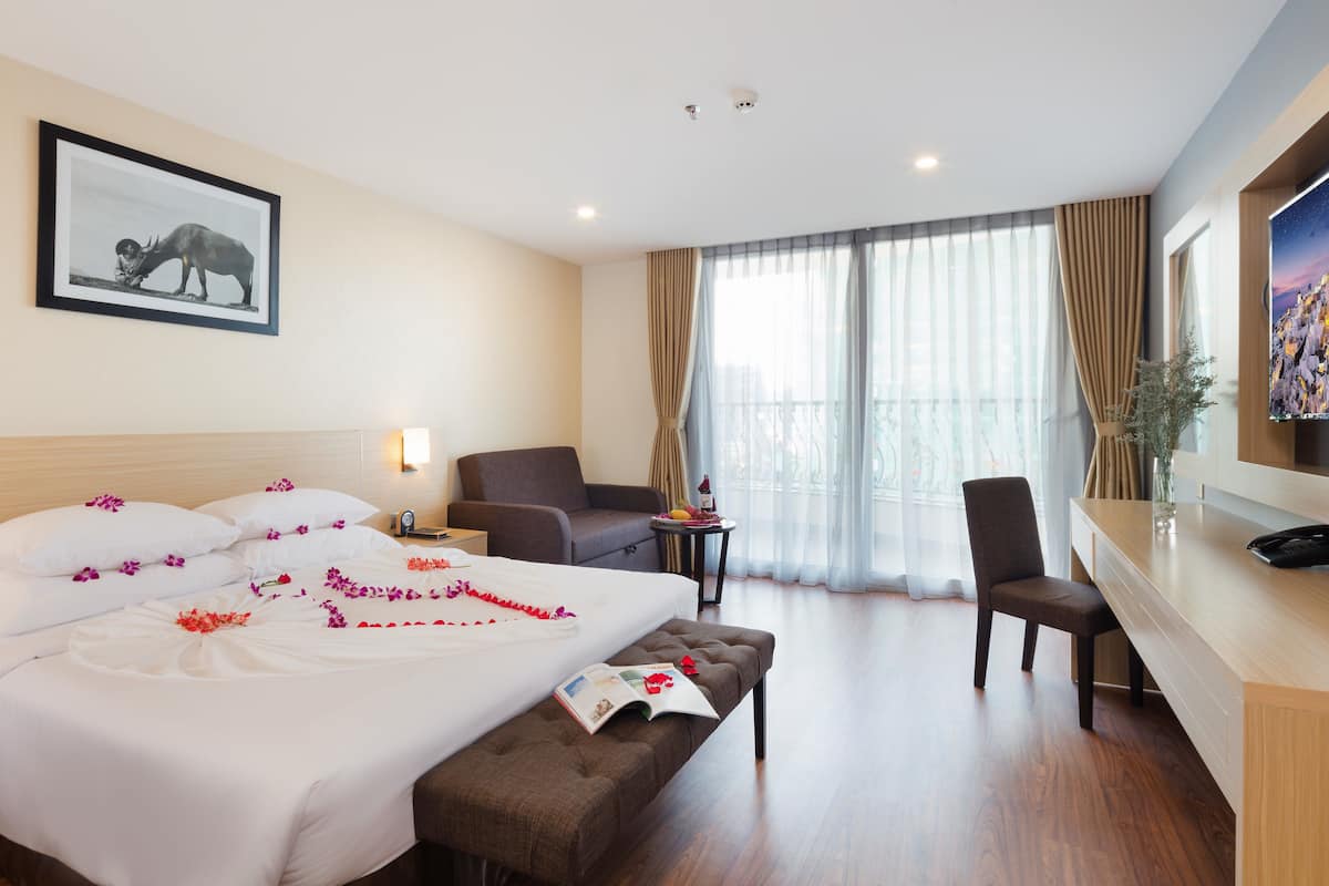 A hotel room with a large bed, a desk, a chair, and a television.