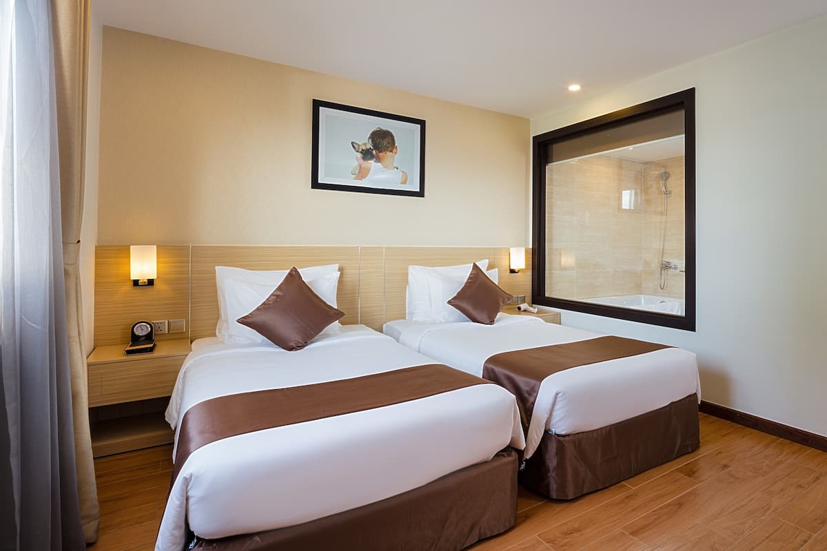 A hotel room with two beds, a large mirror, a framed picture on the wall, and a nightstand with a lamp.