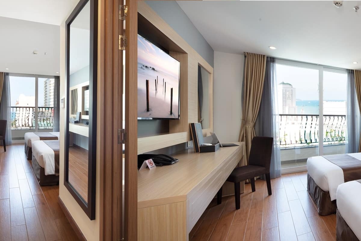 A hotel room with two beds, a desk, a TV, and a balcony with a view.