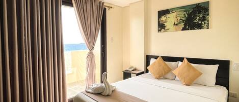 A hotel room with a large bed, a view of the sea, and a painting on the wall.