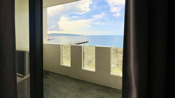 A room with a large window overlooking a body of water, a view of the sea, and a dock with boats. - Navarro Hotel (Malay)