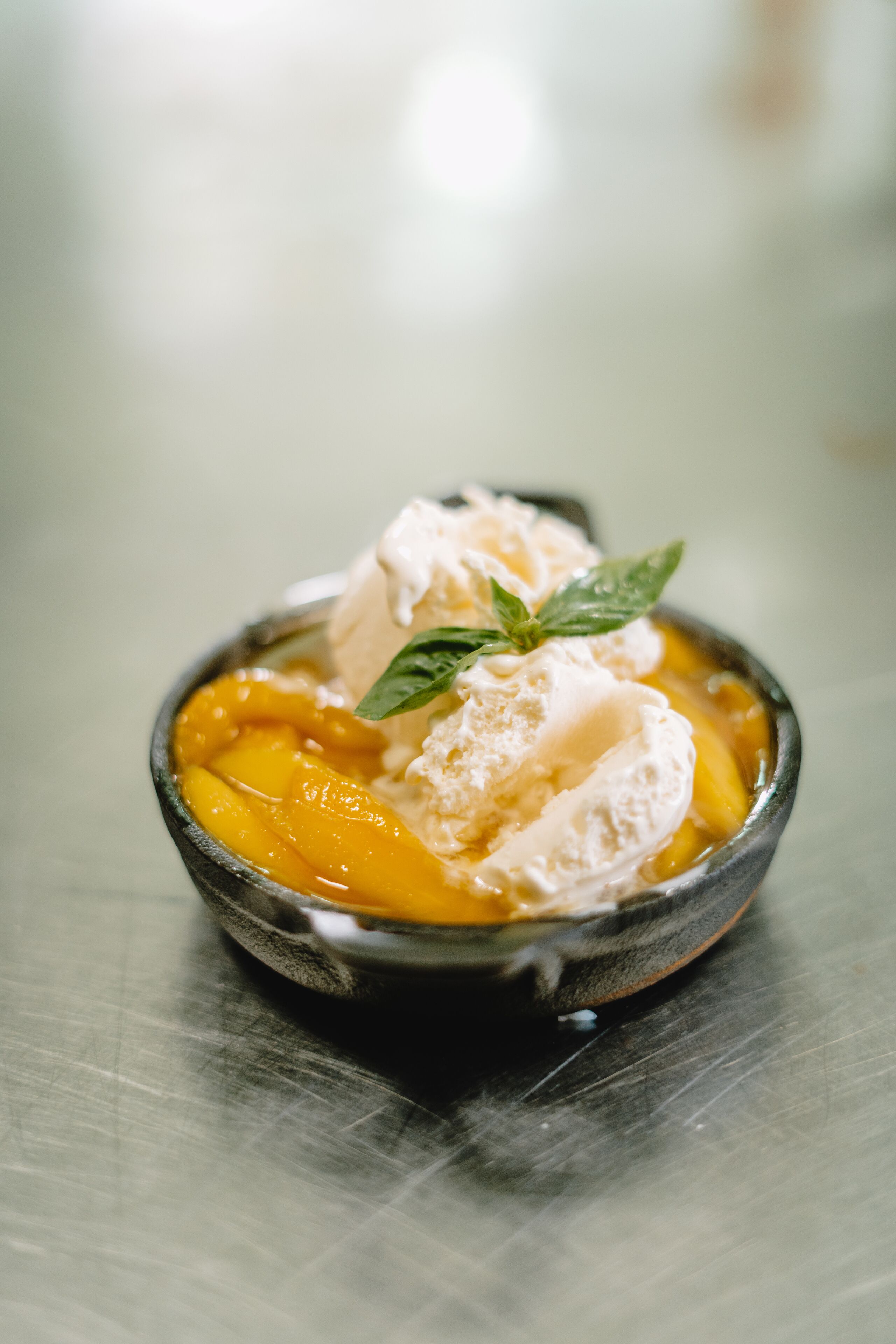 Un tazón de postre de melocotones con helado y una hoja de menta.
