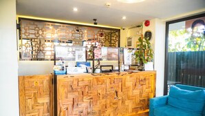 A reception desk with a wooden herringbone pattern, a blue sofa, and a decorative plant. - Navarro Hotel (Malay)