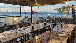 A restaurant with wooden tables and chairs, a view of the water, and string lights on the ceiling. - Navarro Hotel (Malay)