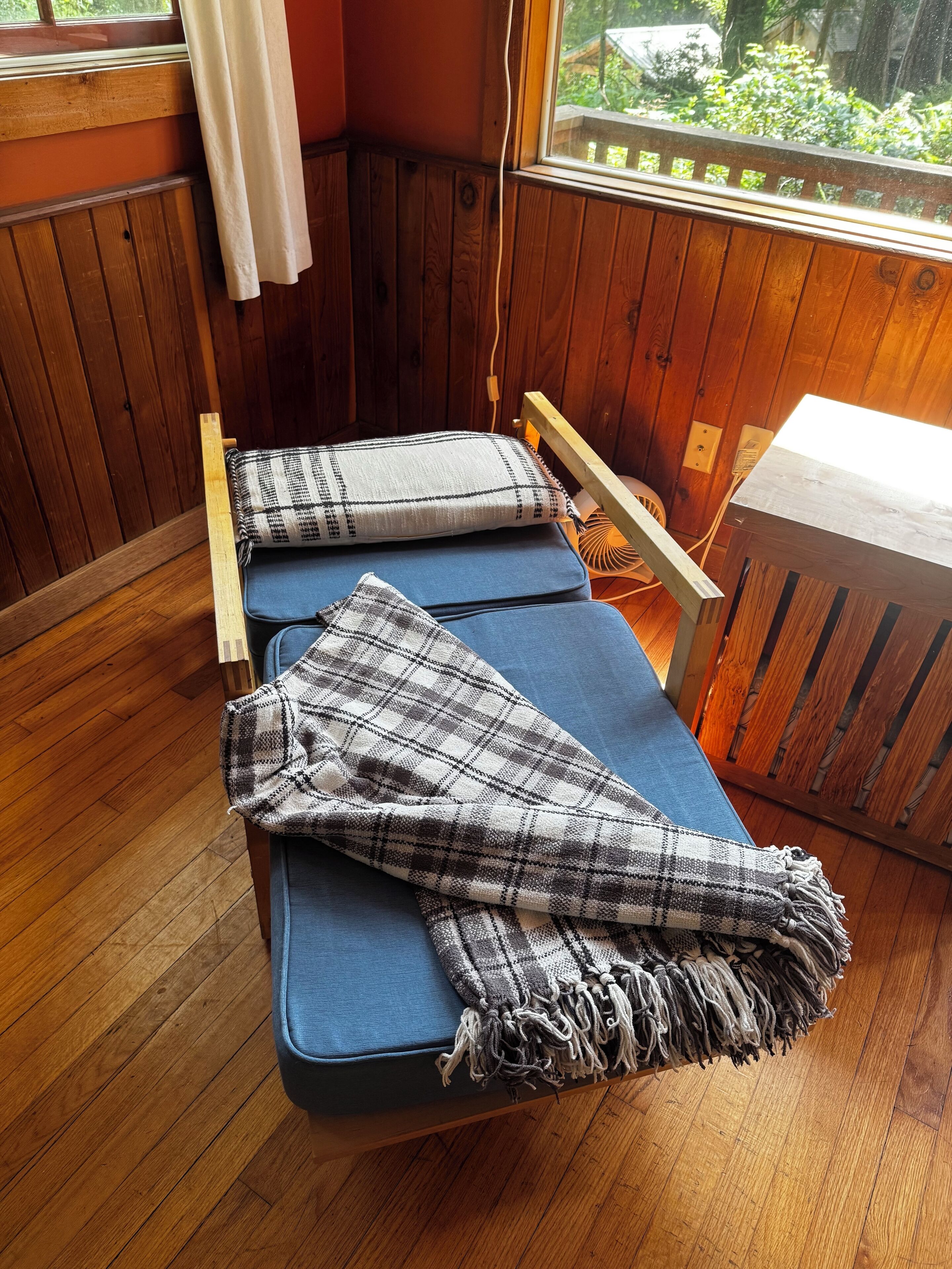 Ein Zimmer mit Holzboden, einem Einzelbett, einem kleinen Tisch und einem Fenster mit Blick auf Grünflächen.