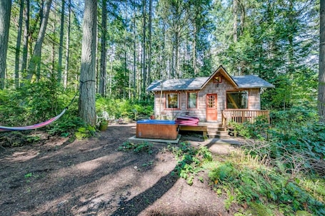 A cabin with a hot tub, surrounded by a forest.
