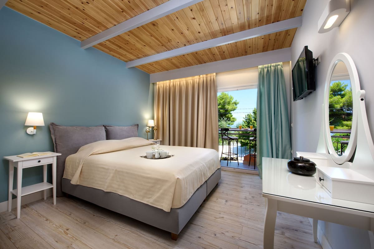 A bedroom with a bed, bedside tables, a TV, a mirror, and a balcony with curtains.