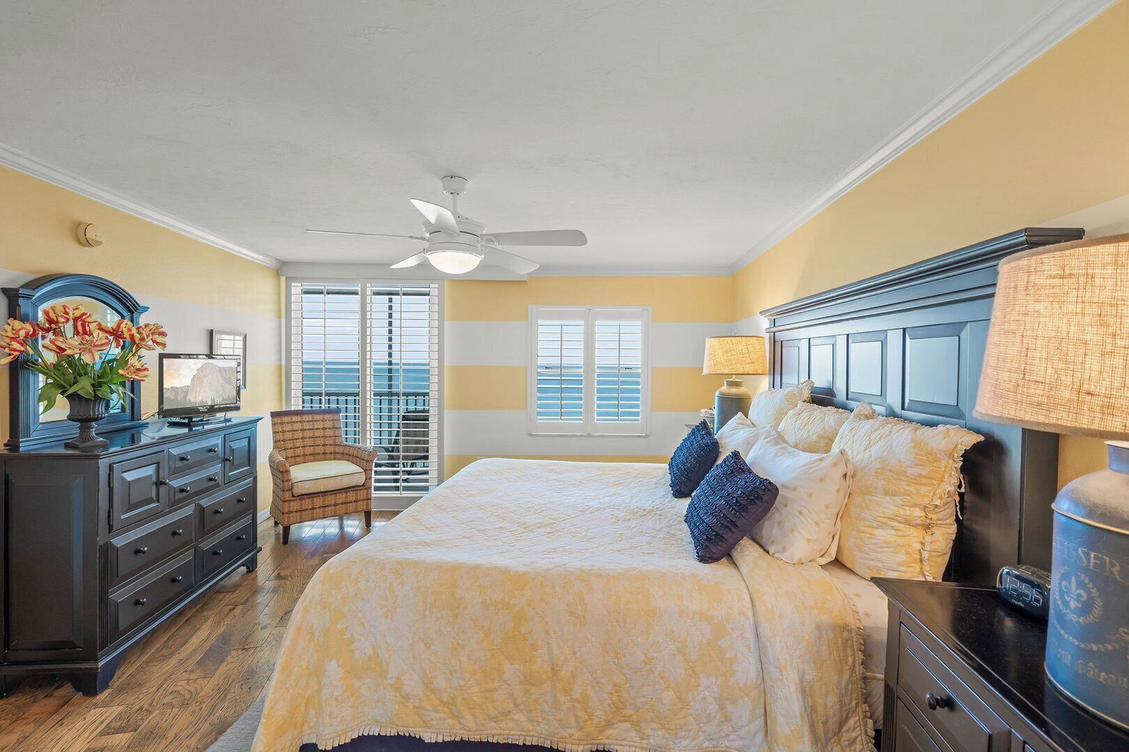 A bedroom with a bed, a dresser, a chair, a ceiling fan, and a window with blinds.