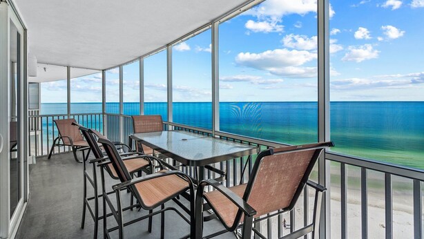A balcony with a table and chairs, large windows, and a view of the ocean. - Crystal Sands Tower Unit 1204 - Beachfront (SARASOTA)