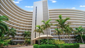 A modern hotel with a curved facade, multiple balconies, and a central vertical tower. - Crystal Sands Tower Unit 1204 - Beachfront (SARASOTA)