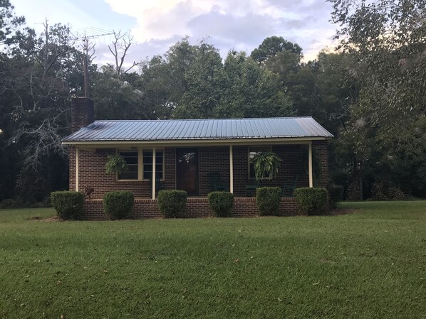 A small brick house with a metal roof, surrounded by a well-maintained lawn and dense trees. - Hillbilly Hut of South Georgia  (Pitts)