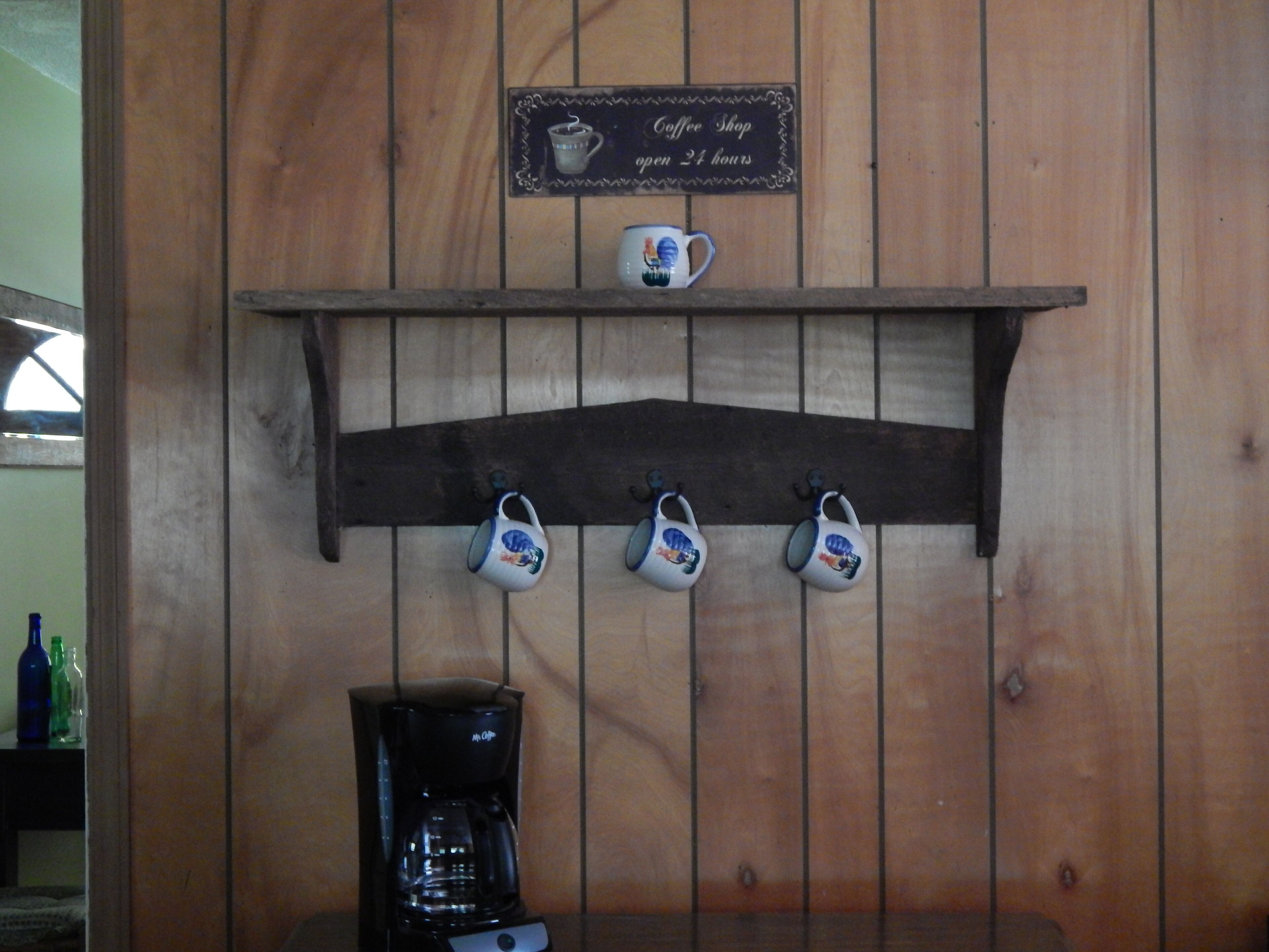 Een bord van een koffiehuis, een plank met mokken en een koffiezetapparaat.