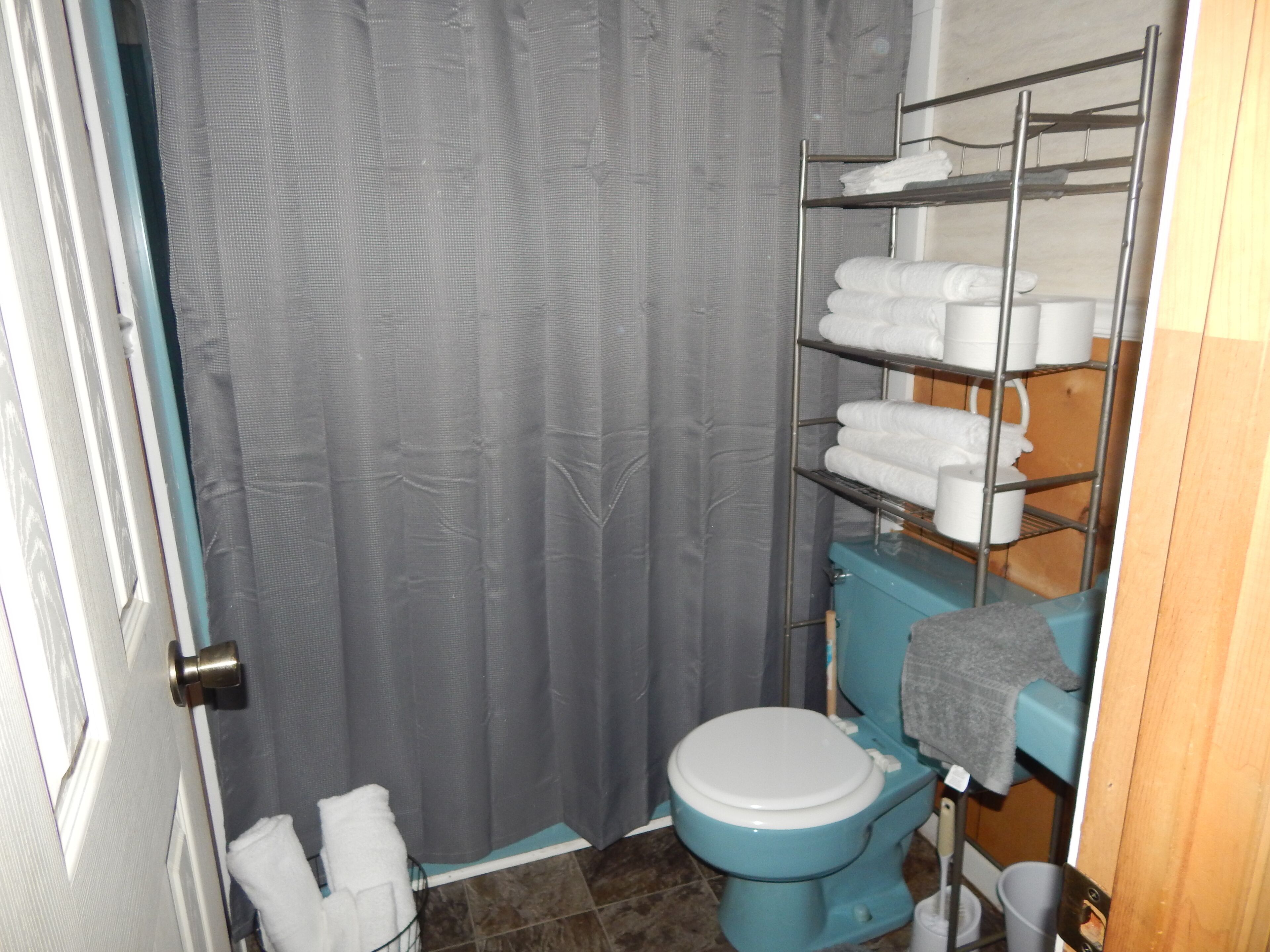 A bathroom with a toilet, a shower curtain, and a shelf with towels.