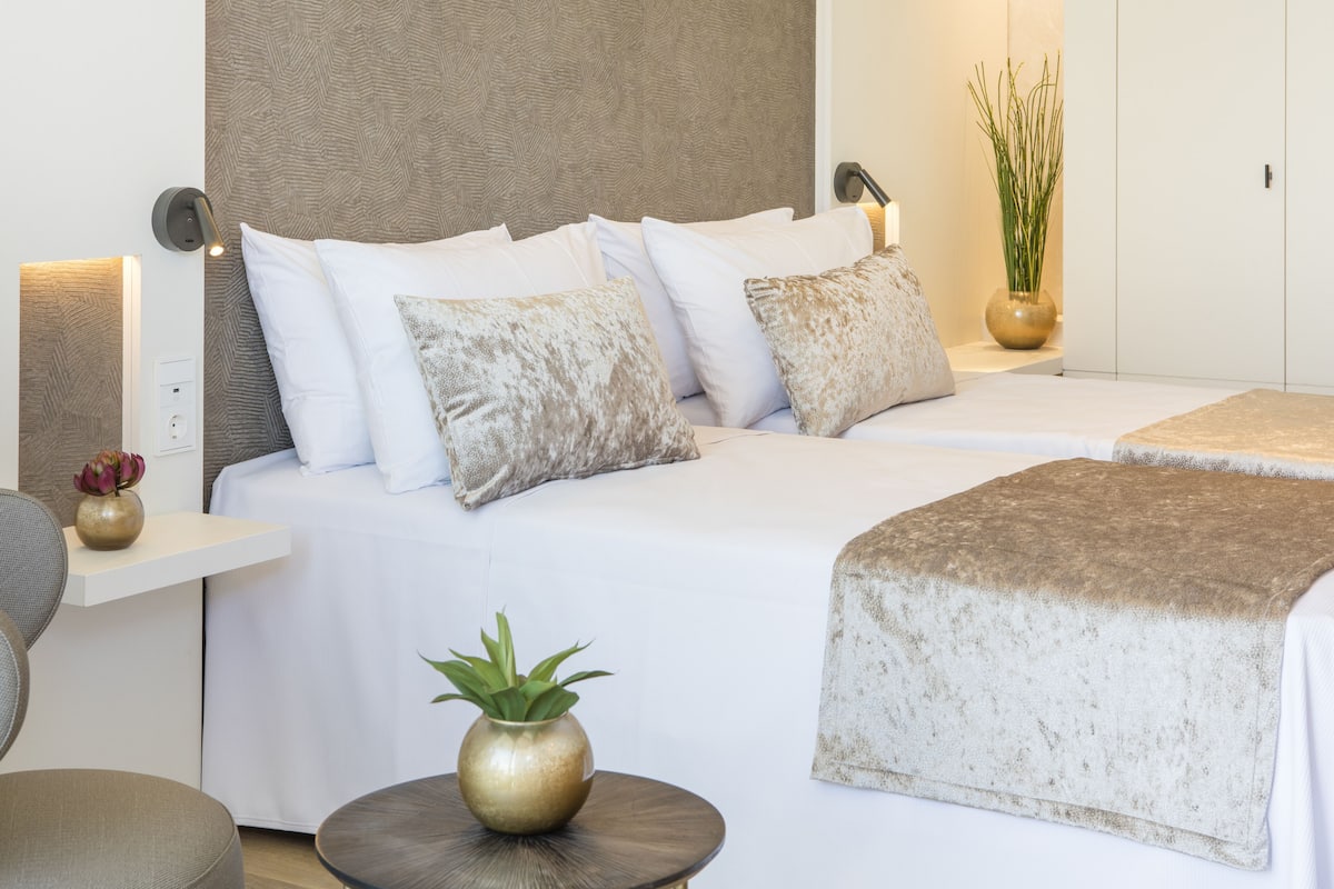 Une chambre d’hôtel avec un lit, des tables de chevet, une lampe, un vase avec des fleurs et une plante en pot.