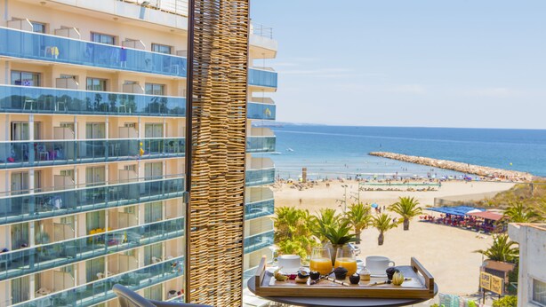 Un balcon avec un plateau de petit-déjeuner, une vue sur une plage et un immeuble de grande hauteur doté de balcons.
