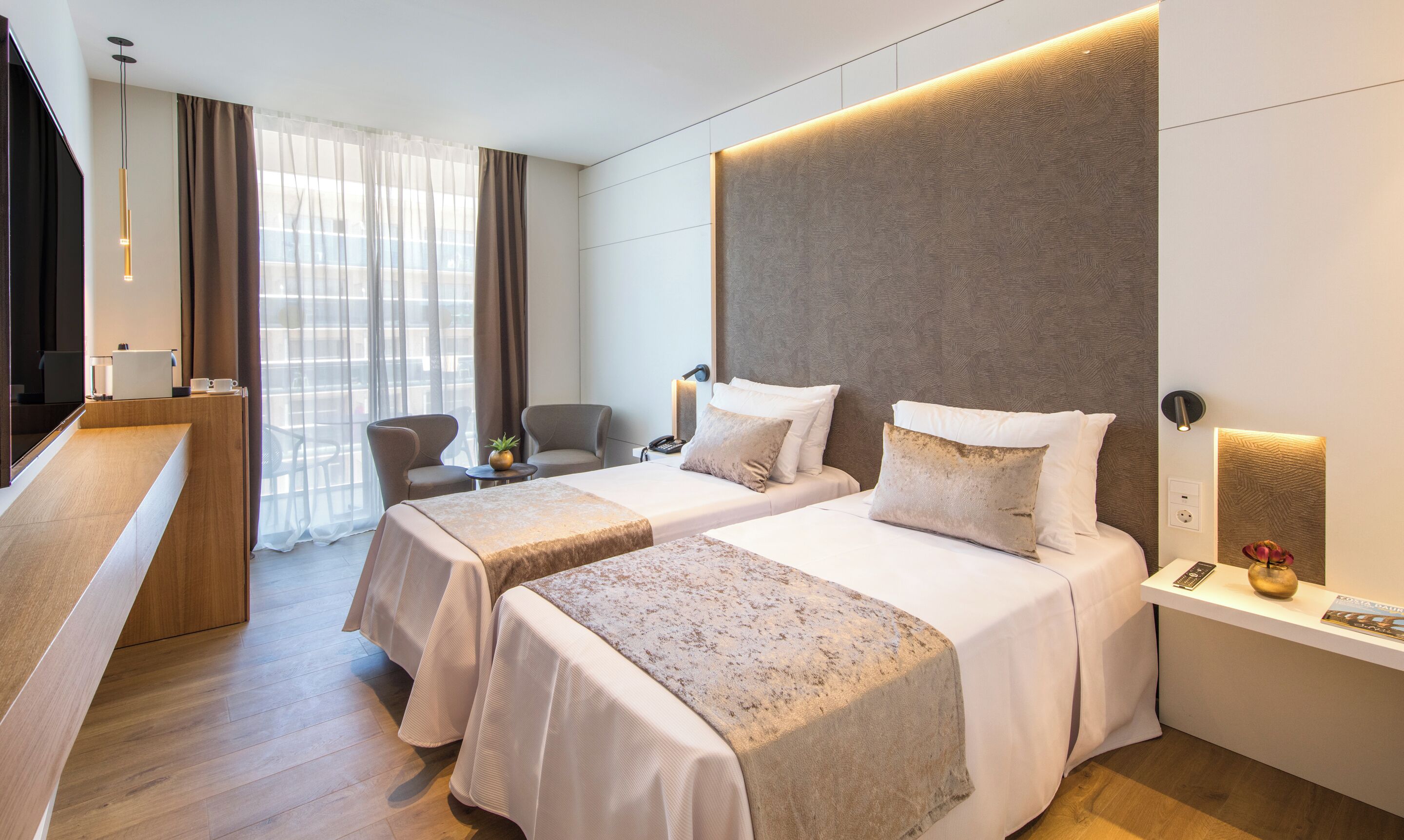 A hotel room with two beds, a desk, a chair, a TV, and a window with curtains.