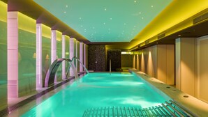 Une piscine intérieure moderne, avec de l’eau cristalline, un escalier en métal et un plafond orné de lumières en forme d’étoiles.